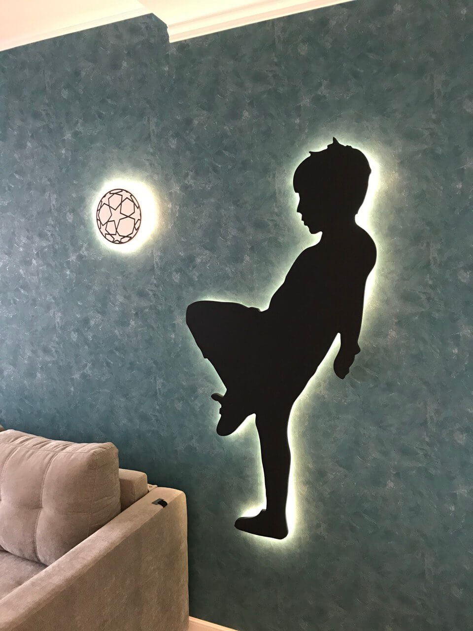 на фото светилиник на стенке в детской комнате. Он сделан в форме мальчика который пинает футбольный мяч